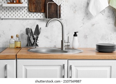 Wooden counter with silver sink and utensils near light wall in kitchen