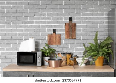 Wooden countertop with microwave oven, houseplants and utensils in modern kitchen - Powered by Shutterstock