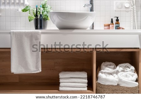 Wooden countertop with shelf for storage fresh and white terry towels. Wicker laundry basket under washbasin in modern hotel bathroom. Clean textile for body hygiene in comfort apartment