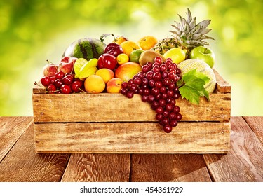 Wooden crate filled with a wide assortment of fresh healthy tropical fruit on a rustic wood table outdoors with sunlit blurred green background - Powered by Shutterstock