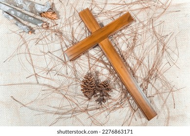 A wooden cross and dry woods used by Catholic Christians on Maundy Thursday and Good Friday on burlap background with pine leaves and pinecones. - Powered by Shutterstock