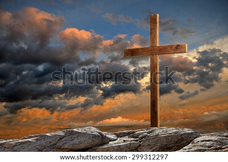 Wooden cross on rocky hill at sunset