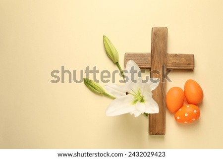 Wooden cross, painted Easter eggs and lily flowers on pale yellow background, flat lay. Space for text