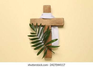 Wooden cross, white cloth and palm leaf on beige background, top view. Easter attributes
