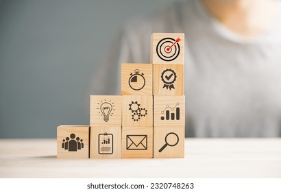 Wooden cube block step on a table with Action Plan, Goal, and Target icons. Success and business target concept. Project management and company strategy symbolize growth. - Shutterstock ID 2320748263