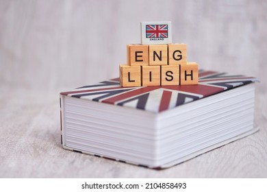 THe wooden cube "ENGLISH" alphabet with the union flag on  the english book. English is the language of science, aviation, computers, diplomacy, and tourism. It's an official language for many countr  - Shutterstock ID 2104858493