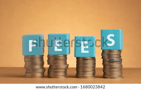 Wooden cube with Fees words on stacked of coins. 