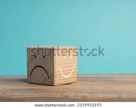 A wooden cube with light and dark side, once with smiling face and with sad face, There is always the option to choose, which face do you choose?