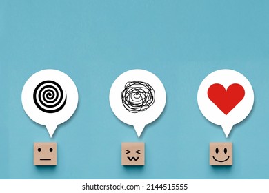 Wooden cube with unhappy face with a tangle of thoughts in its head , wood block with emotion smile happy face and love in thoughts on blue background