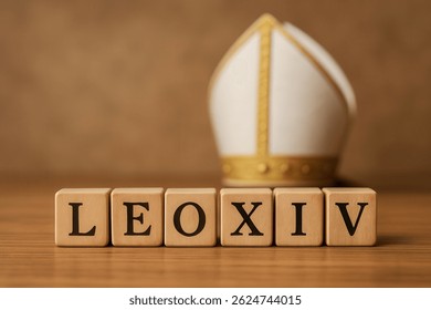 Cubos de madera con letras negras que componen el nombre del Papa León XIV con una mitra blanca y dorada en el fondo, sobre una mesa de madera