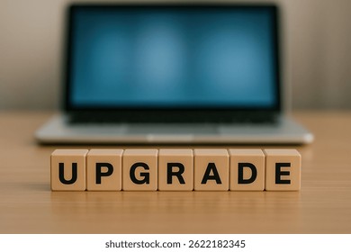 Wooden cubes composing the word upgrade in front of a blurred laptop suggesting a software update or new hardware purchase