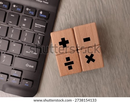 Wooden cubes displaying basic mathematical operator symbols arranged on a surface next to a computer keyboard.