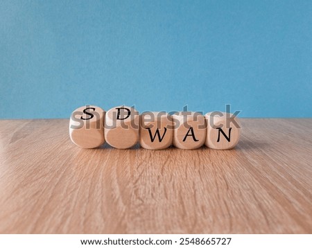 Wooden cubes form the expression SD WAN. Symbol for Software defined Wide Area Networking. Beautiful blue background, wooden table. Copy space.