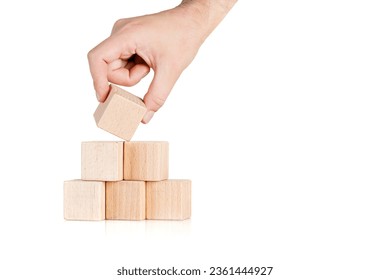 wooden cubes in the form of a pyramid with a hand on an isolate white background close-up - Shutterstock ID 2361444927