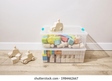 Wooden cubes, kids toy cars sorted in plastic containers, stand on the floor in the nursery room. Concept of making toys from ecological materials, sorting and organizing things, storage, home