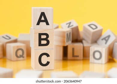 wooden cubes with letters ABC arranged in a vertical pyramid, yellow background, reflection from the surface of the table, business concept, ABC - short for always be closing