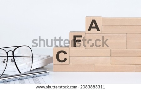 wooden cubes with letters CFA on white table with keyboard and glasses