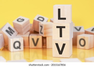wooden cubes with letters LTV arranged in a vertical pyramid, yellow background, reflection from the surface of the table, business concept, LTV - short for lifetime value