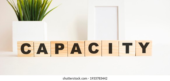 Wooden cubes with letters on a white table. The word is CAPACITY. White background with photo frame, house plant. - Shutterstock ID 1933783442