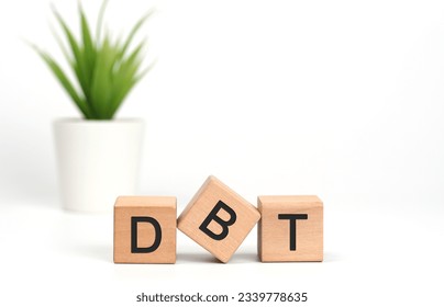 Wooden cubes with letters on white background. The words written is DBT Dialectical Behavior Therapy acronym with a pot of green plant.Psychological treatment concept, stress regulation.Copy space.