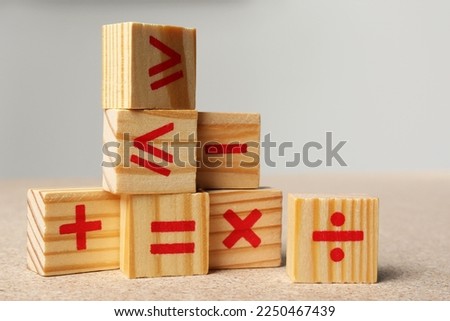 Wooden cubes with mathematical symbols on table against light background