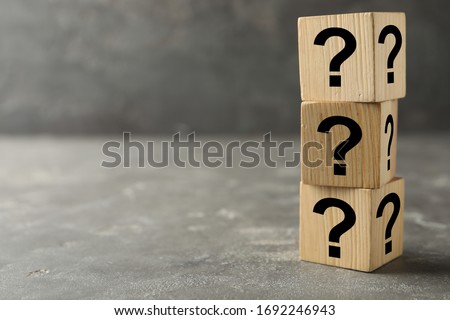 Wooden cubes with question marks on grey stone table. Space for text