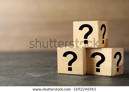 Wooden cubes with question marks on grey stone table, closeup. Space for text