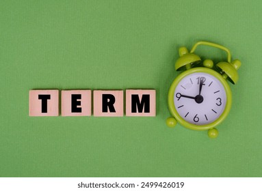 A wooden cubes with text “TERM” on it next to green alarm clock. Discussions about time management, deadlines, or educational terms concept - Powered by Shutterstock