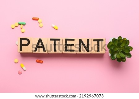 Wooden cubes with word PATENT and pills on pink background