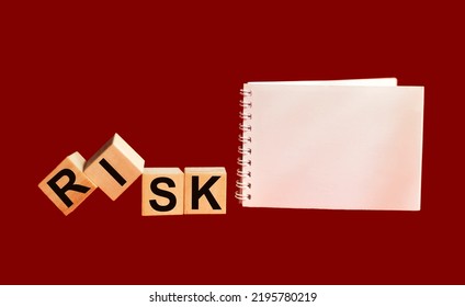 Wooden Cubes With The Word Risk On A Red Background With A Notepad. Risk Acceptance, Risk Management Or Evaluation Concept. Eliminate Risks When Making Business Financing Decisions.