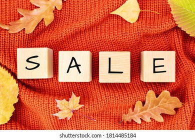 Wooden cubes with the word SALE and yellow fallen maple leaves around on an orange knitted sweater. Colorful concept of discount season, shopping background.