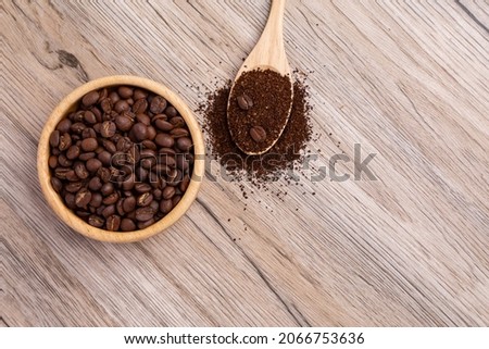 A wooden cup holds coffee beans, and a wooden spoon has ground coffee.