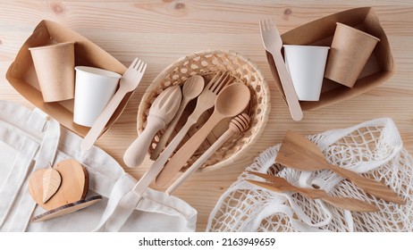 Wooden cutlery, paper disposable tableware and mesh bag. Eco friendly kitchen utensils and linen shopping bag on a wooden table. Zero waste or plastic free concept