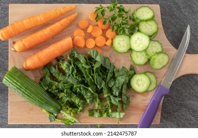 Wooden cutting board with fresh organic vegetables and knife. Top view, close-up. Chopped spinach, sliced cucumber, and carrot for salad. Eating healthy food concept. Flat lay.