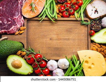 Wooden cutting board and ketogenic low carbs ingredients for healthy weight loss diet, top view, copy space. Keto foods: meat, fish, avocado, cheese, vegetables, nuts. Clean eating, healthy fats 