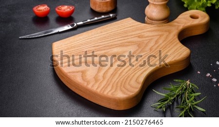 A wooden cutting board with a kitchen knife with spices and herbs on a dark concrete background. Cooking at home