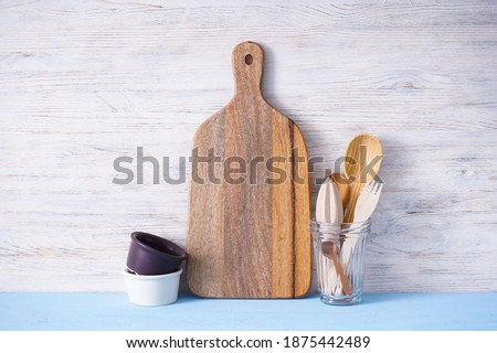 Wooden cutting board and kitchen utensils on wooden background, place for text.