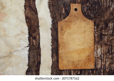 Wooden Cutting Board And Old Tattered Fabric On A Textured Wooden Background. Burnt Cracked Wood. Top View. Selective Focus