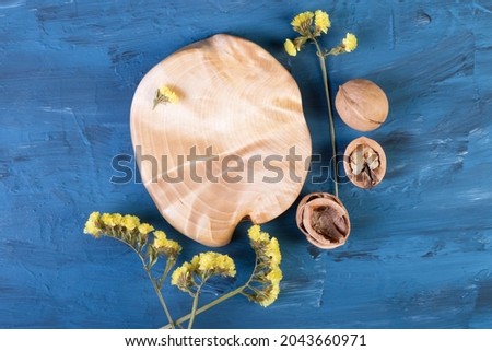 a wooden cutting board on a blue concrete table. dishes for serving. walnuts, walnut shells and yellow dried flowers. top view.he was lying flat. Wooden plate, a place to copy.