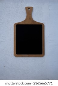 Wooden cutting board on white concrete wall. Vertical photo. Black chalk board. Copy space for text. Concept for street cafe menu, catering, offer, cafe, pub, bar, food, restaurant, cooking. Copyspace - Shutterstock ID 2365665771