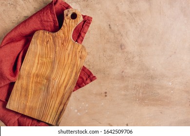 Wooden Cutting Board Over Towel On Beige Rustic Kitchen Table. Space For Your Recipe Or Menu. Top View.