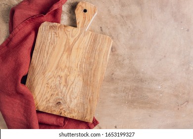 Wooden Cutting Board Over Towel On Beige Rustic Kitchen Table. Space For Your Recipe Or Menu. Top View.