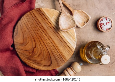 Wooden Cutting Board Over Towel With Utensils On Beige Rustic Kitchen Table. Space For Your Recipe Or Menu. Top View.