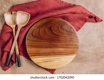 Wooden Cutting Board Over Towel With Utensils On Beige Rustic Kitchen Table. Space For Your Recipe Or Menu. Top View.