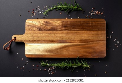 Wooden cutting board with pepper,salt and fresh rosemary on a black background, copy space - Powered by Shutterstock