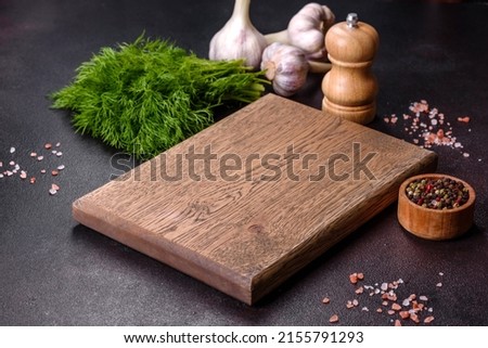 A wooden cutting board with spices, herbs, cherry tomatoes and salt on a black concrete background. Cooking at home