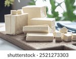 A wooden cutting board with a variety of white blocks of tofu on it. The blocks are cut into different shapes and sizes, and they are arranged in a way that creates a visually interesting display