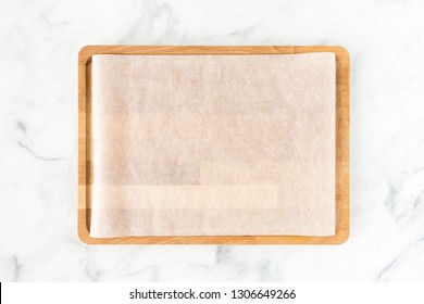 Wooden cutting board with white parchment paper on white marble background with lots of copy space. Top view.