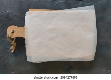 Wooden cutting board and white parchment paper on dark gray background. Mockup for recipes, shopping list or food