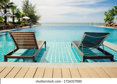 Wooden daybed place on tile floor in swimming pool with seascape view in background.